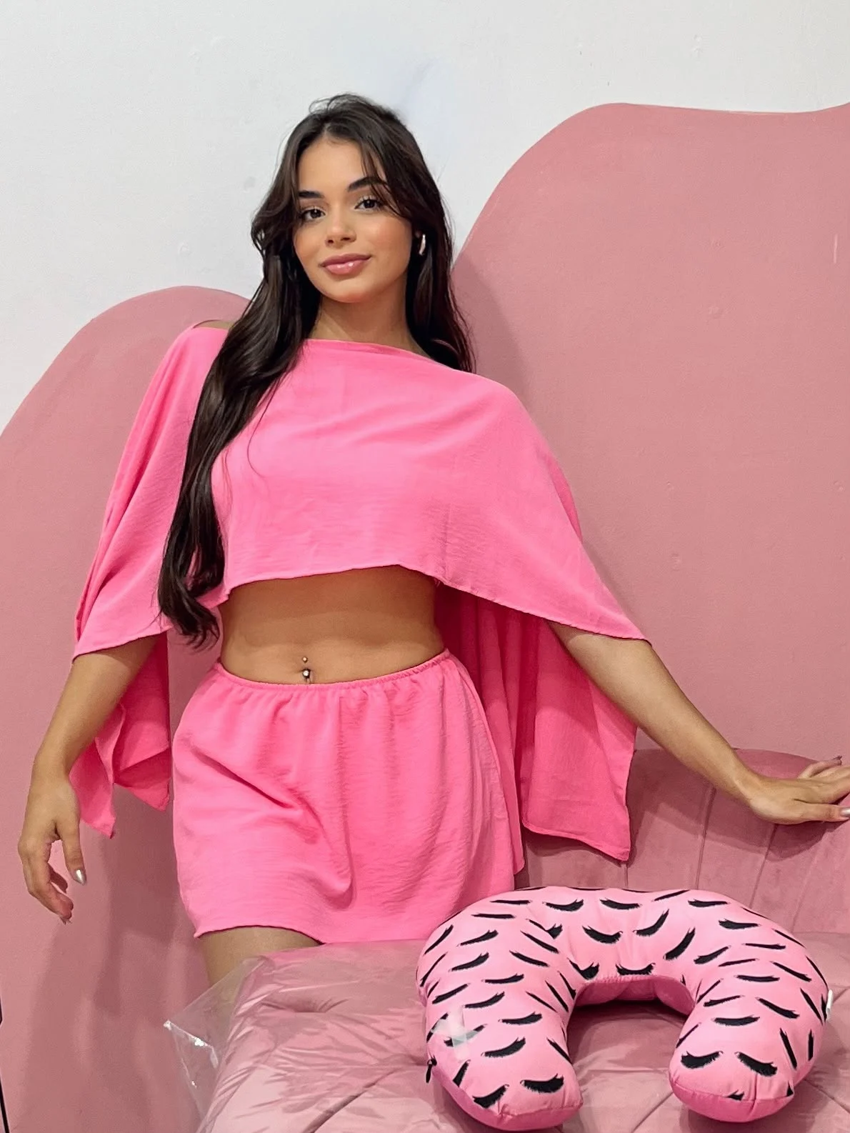 Giovana em seu estúdio, vestindo um conjunto rosa, ao lado da maca de atendimento